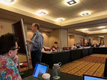 Scott writing on a flip chart during a trainer gathering Tim is in the foreground